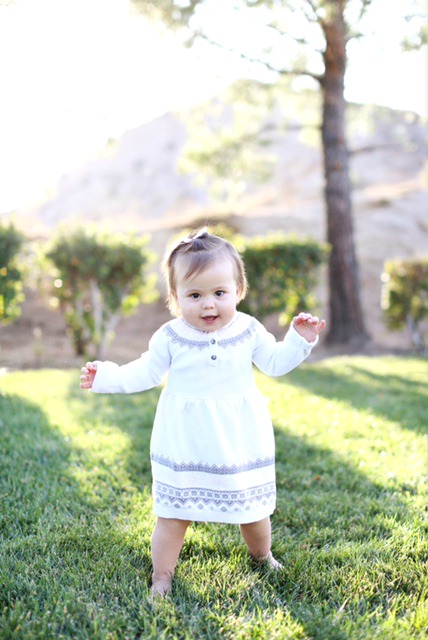 A baby girl standing in a grassy area