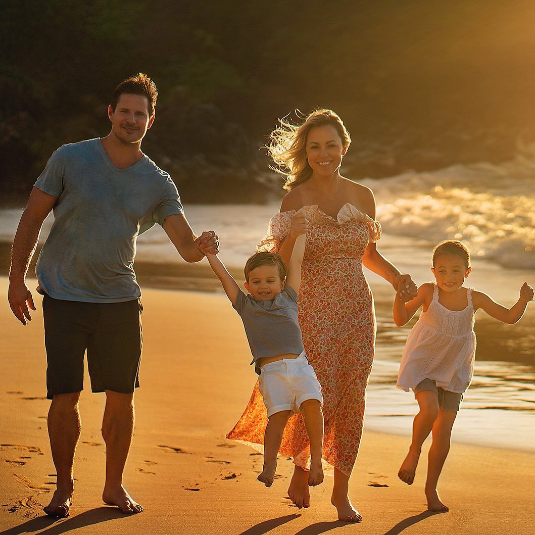 Family of four - dad, mom, son, and daughter - on the beach running by the surf. 