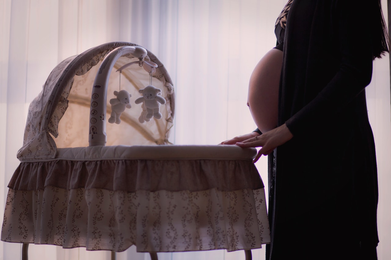 Pregnant woman standing next to a bassinet.