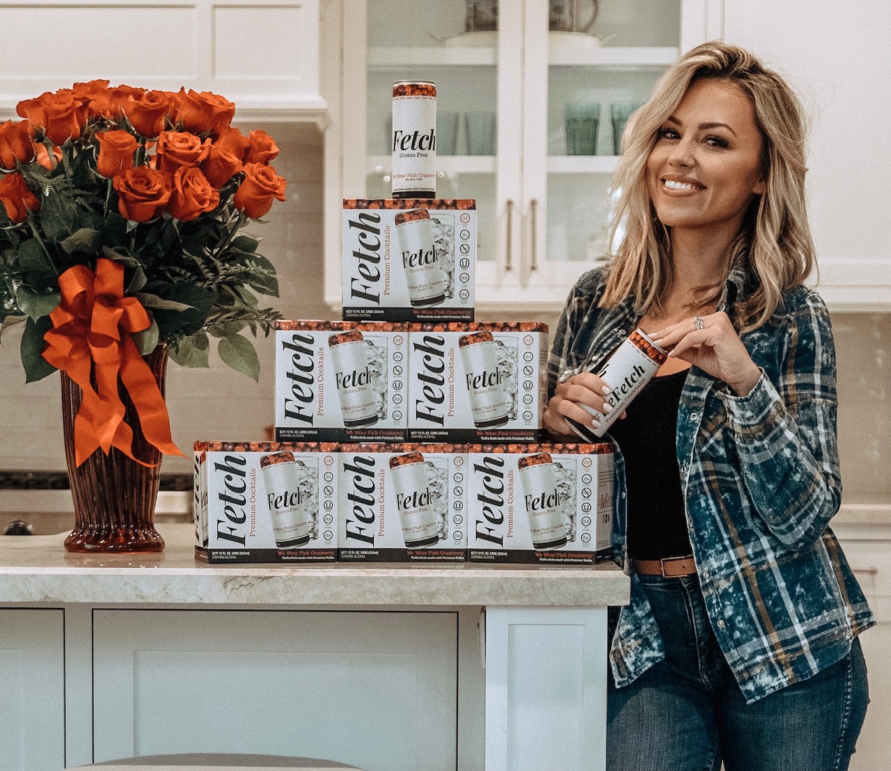 Jessica Hall standing in her kitchen with boxes of Fetch canned cocktails on her counter next to her.