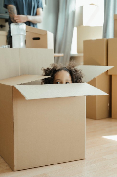 Boxes stacked in living room with a kid peeking out of one.