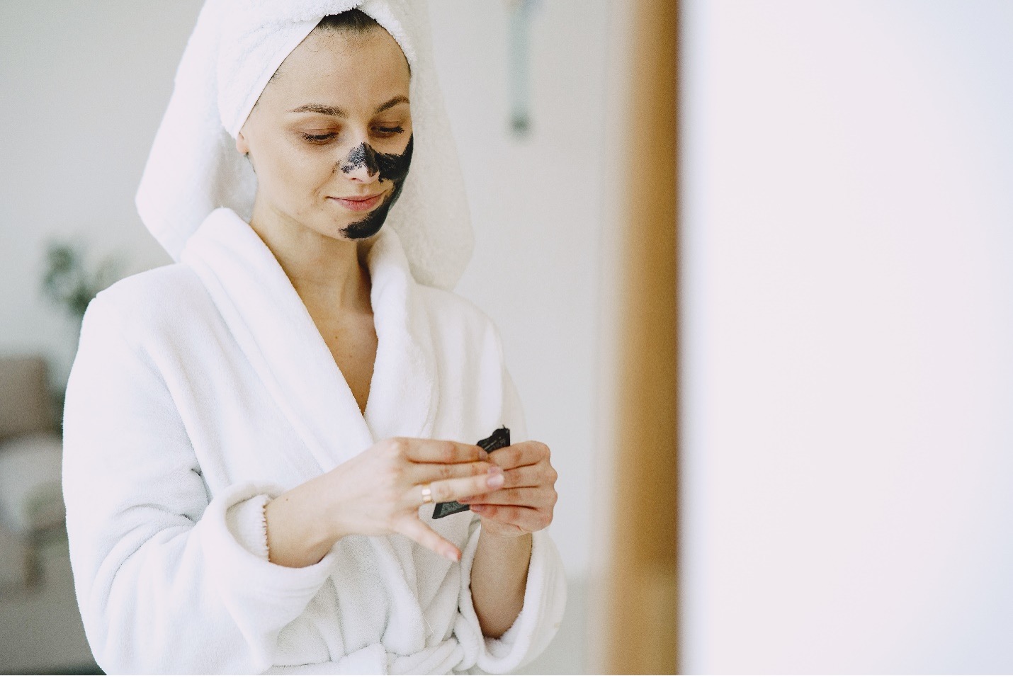 Woman applying face mask wearing a bathrobe and towel on her head.