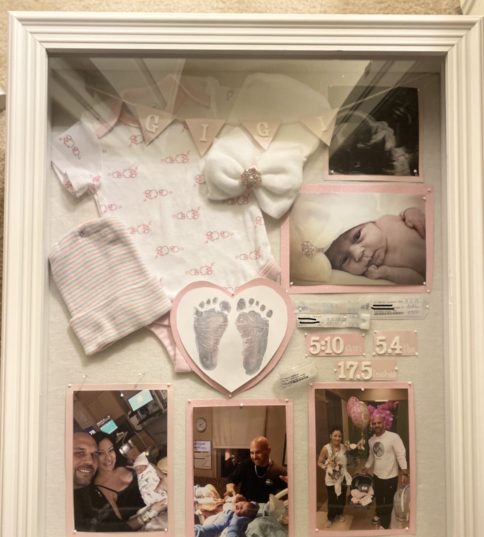 Shadow box with white frame filled with baby momentos and pictures.