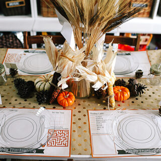 Table set for Thanksgiving, with printable placemats for kids that have games and sections to draw and a centerpiece of pumpkins and wheat stalks.