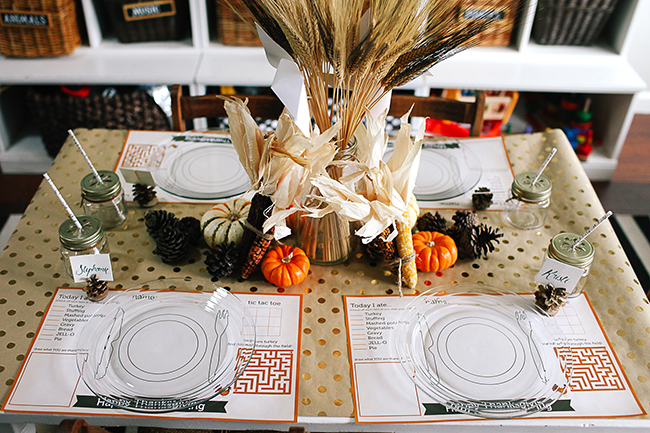 Table set for Thanksgiving, with printable placemats for kids that have games and sections to draw and a centerpiece of pumpkins and wheat stalks.