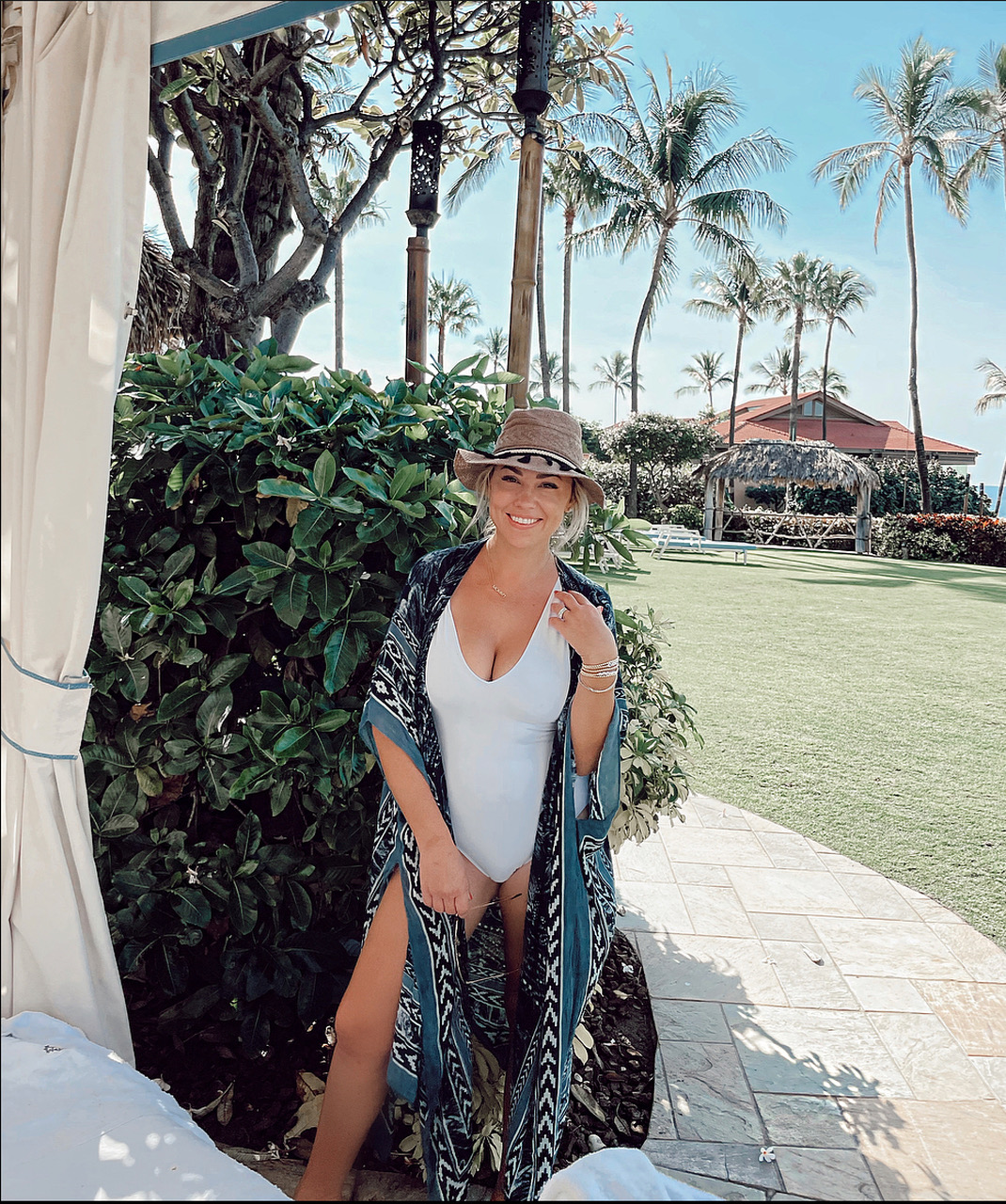 Jessica in a white bathing suit with green coverup adn hat standing by a cabana at the Four Seasons Maui.