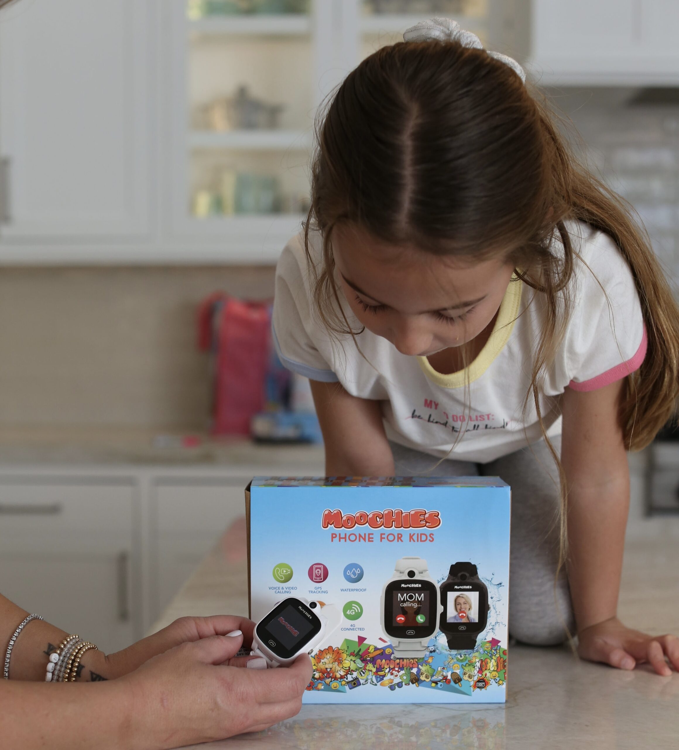 Girl sitting on counter looking at Moochies phone watch box. 