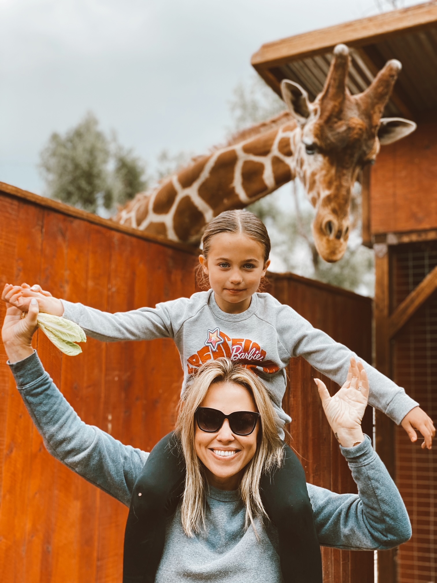 Jessica Hall with daughter sophie on her shoulders and a giraffe peaking over from behind. 