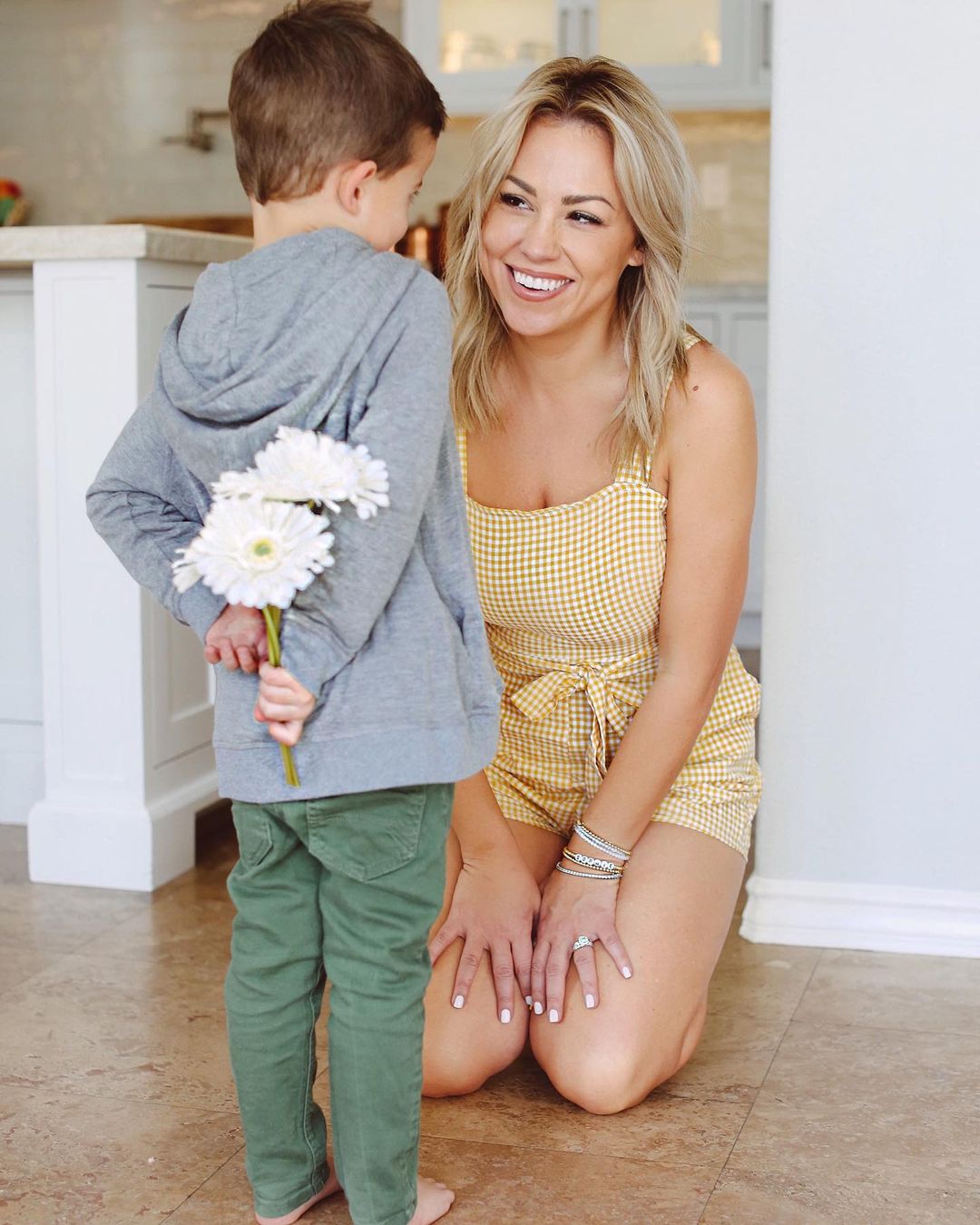 Jessica kneeling on the floor in front of her son who is holding white flowers behind his back.