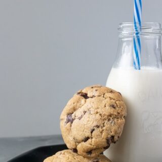 Chocolate chip cookies sitting on a plate with a glass bottle of milk.