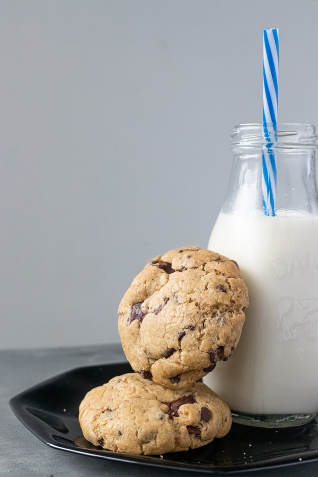 Chocolate chip cookies sitting on a plate with a glass bottle of milk.